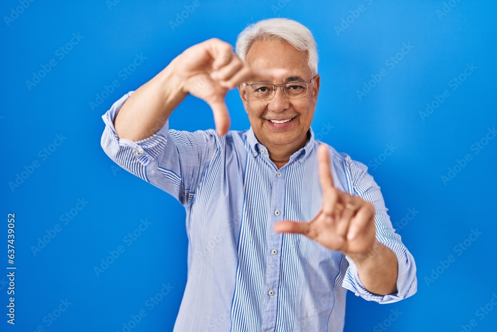 Fototapeta premium Hispanic senior man wearing glasses smiling making frame with hands and fingers with happy face. creativity and photography concept.