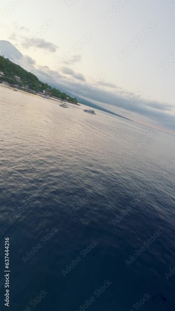 Vertical video. FPV sport drone moving over rippling sea bay with floating yachts located mountain covered greenery jungle. Aerial low dynamic sunset island blue ocean water calm summer evening resort Vertical video. FPV sport drone moving over rippling sea bay with floating yachts located mountain covered greenery jungle. Aerial low dynamic sunset island blue ocean water calm summer evening resort