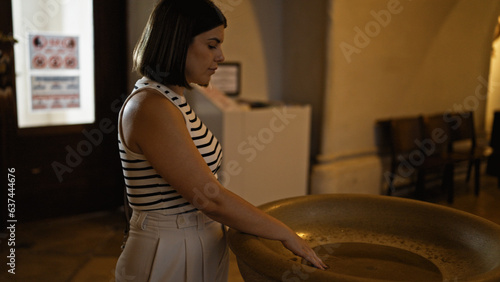 Young beautiful hispanic woman praying with holy water at Augustinian Church in Vienna