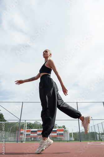 A blonde woman with a short haircut shows her agility and fitness as she jumps on a running track. She wears a black outfit and white sneakers