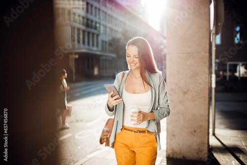 Young woman using a smart phone while walking on a sidewalk in the city
