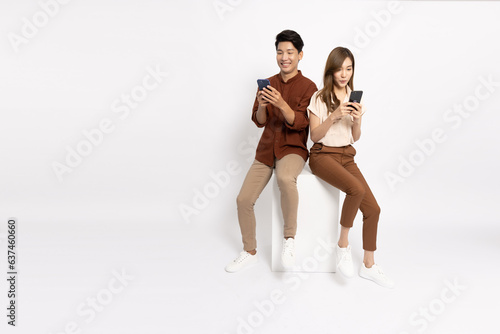 Asian couple sitting on white box and typing smartphone isolated on white background
