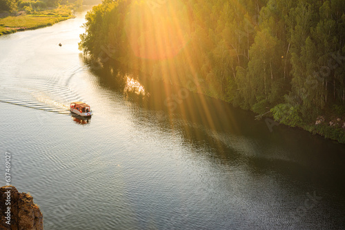 the boat floats on the river on a summer evening in the rays of the sun. forest along the banks of the river