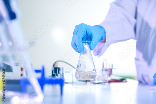 Woman chemist hand in plastic glove shaking laboratory beaker. Scientific Lab for Medicine, Biotechnology Researchers.
