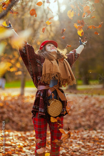 smiling stylish female in red hat throwing autumn leafs