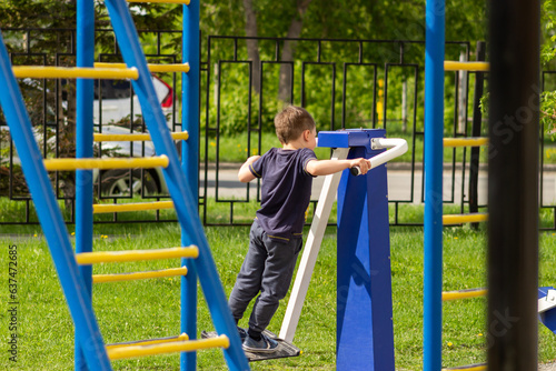A little caucasian athletic boy works out on a street simulator on the playground. A sporty child does exercises in kindergarten. Sports and activities. Healthy lifestyle. Sunny summer day