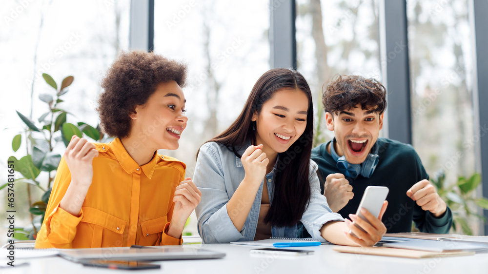 Obraz premium Excited multiracial students looking at cellphone and clenching fists, checking exams results online in classroom