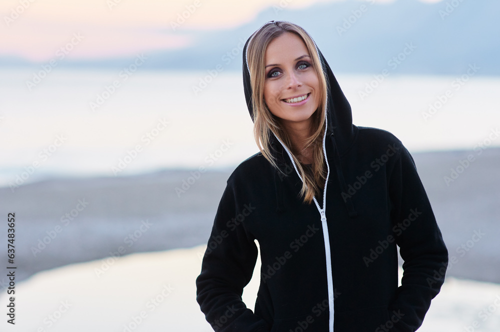 Beauty casual look. Young smiling woman in black hood over the dusk sky and sea. Beauty casual look. Young smiling woman in black hood over the dusk sky and sea.