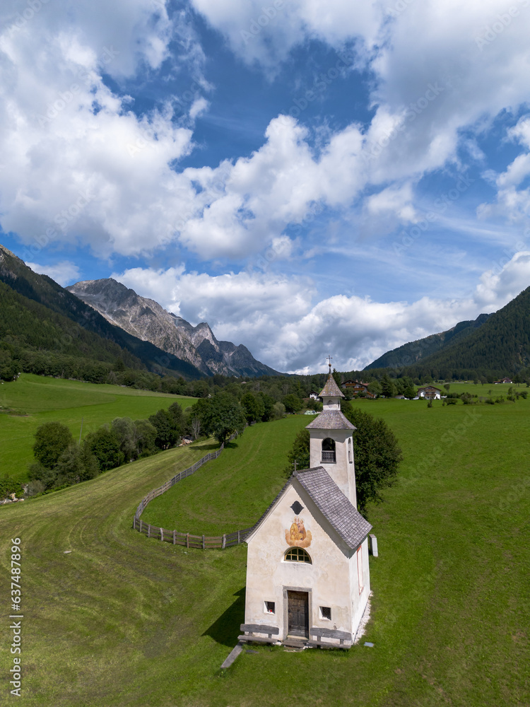 Small white alpine chapel on green field of grass in valley between rocky mountain alp tops in Italian Dolomite mountain range 