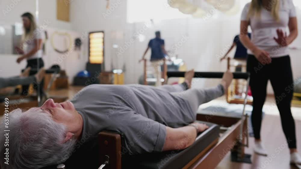 Older Woman Stretching on Pilates Machine under Guidance of Female Coach, Senior Person Engaging in Exercise during Studio Session Older Woman Stretching on Pilates Machine under Guidance of Female Coach, Senior Person Engaging in Exercise during Studio Session