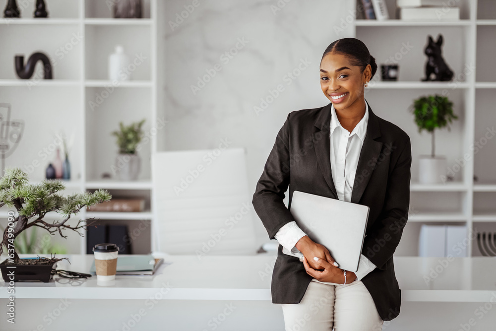 Successful business person. Portrait of happy black businesswoman with laptop in hands leaning at table in office Successful business person. Portrait of happy black businesswoman with laptop in hands leaning at table in office