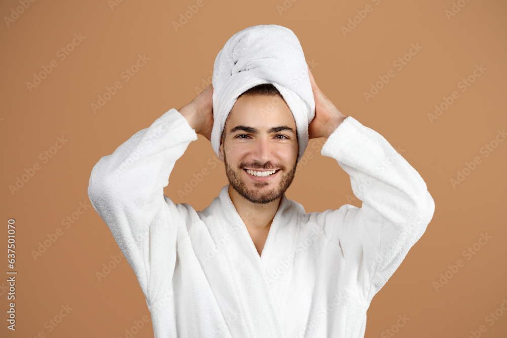 Guy Touching Towel On Head, Wearing Bathrobe Over Beige Background Guy Touching Towel On Head, Wearing Bathrobe Over Beige Background