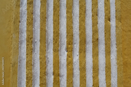 Mur ancien décoré de lignes verticales jaunes en relief.