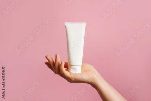 Woman hand holding unbranded white tube with cosmetic cream on pink background. skin care concept, copy space