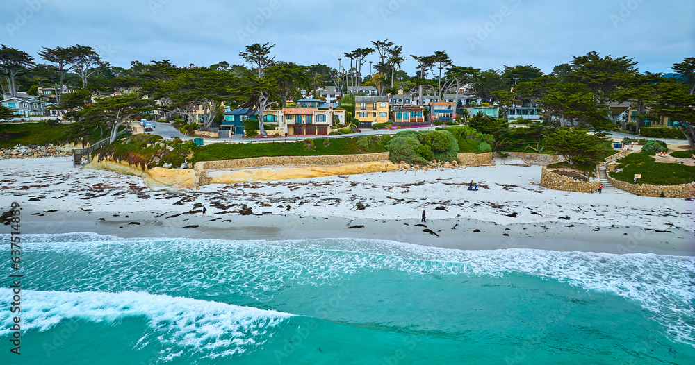 Gorgeous turquoise waves crashing against Carmel Beach shore with kelp on white sand aerial
