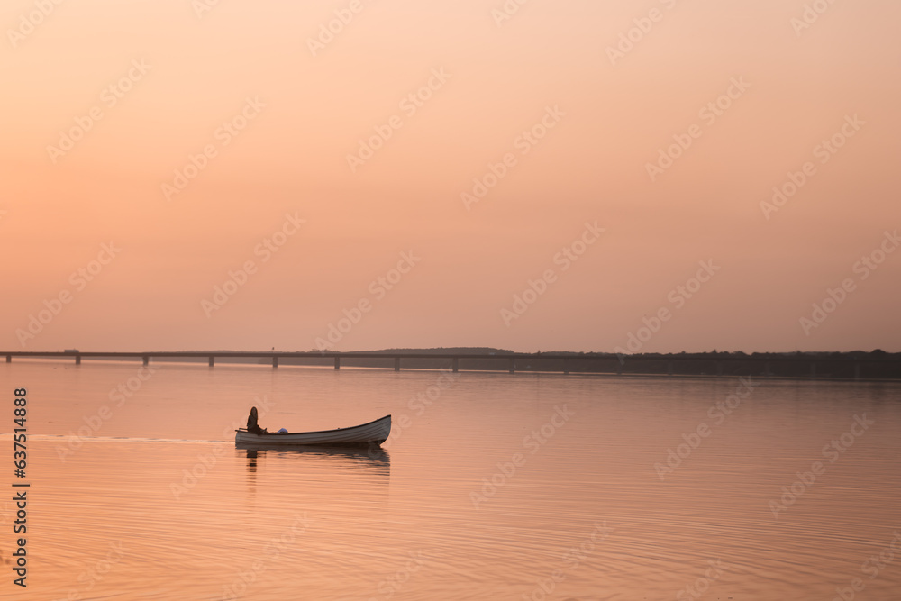 Lonely sailor in golden sunset lighting, sailing in small boat on the lake.