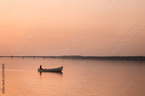 Lonely sailor in golden sunset lighting, sailing in small boat on the lake. © Mads