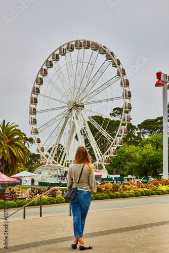 Woman in blue jeans and tan top with black purse looking at the SkyStar Wheel Ferris wheel