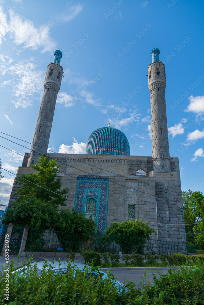Obraz premium Side view of old Saint Petersburg Mosque with blue dome and stone minarets against clear blue sky with white clouds in a sunny summer morning. Religious architecture. Muslim culture theme.