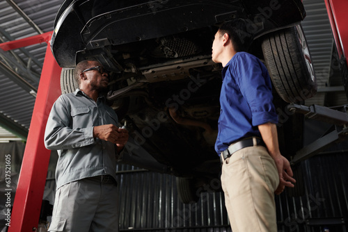 Car owner and mechanic standing under suspended car and discussing what needs to be fixed © DragonImages