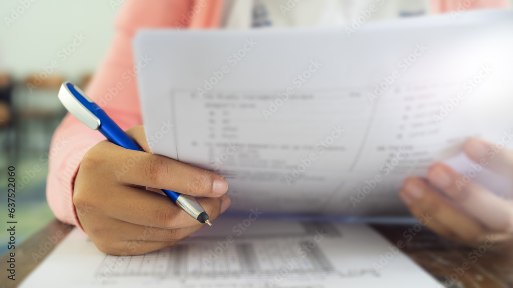 Close up hand of students reading and taking exam sheets exercises answer with stress in classroom Close up hand of students reading and taking exam sheets exercises answer with stress in classroom
