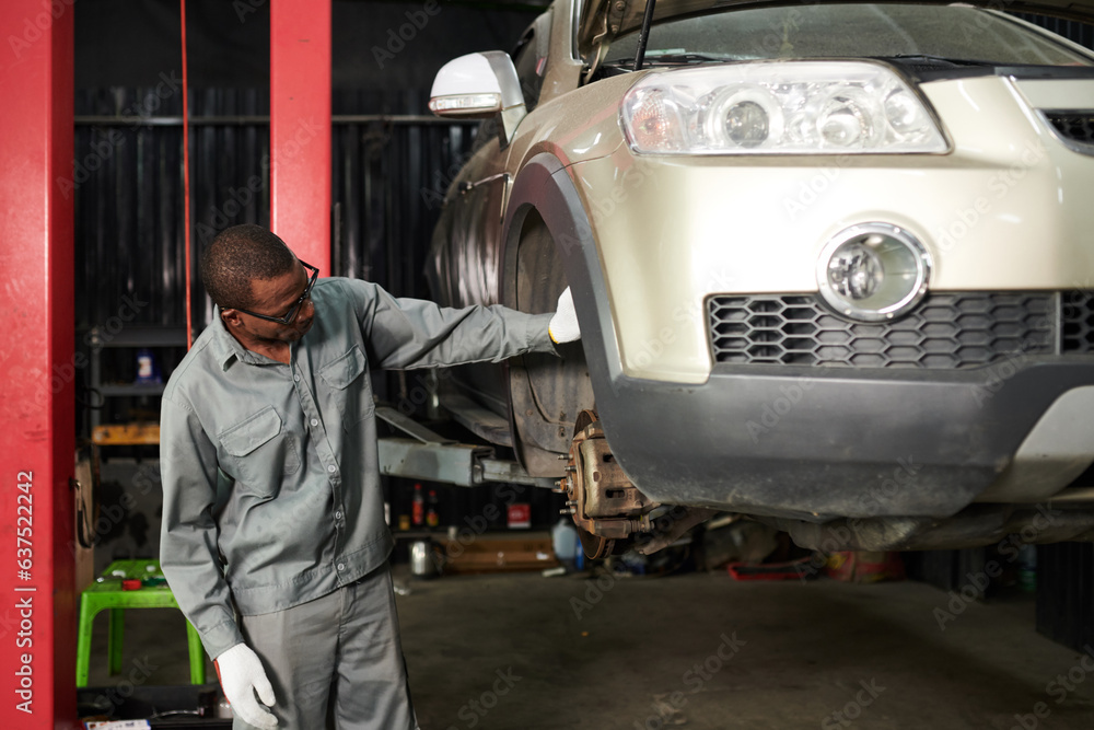 Car mechanic in grey overall examining suspended car