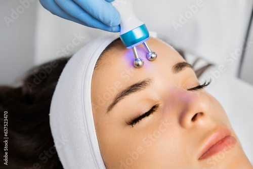 Specialist uses microcurrent massage device on female forehead for removing wrinkles.