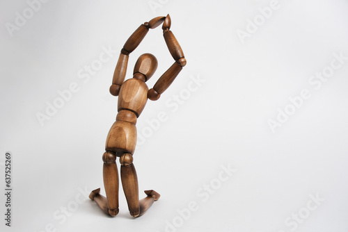 Wooden mannequin pose of praying man, kneeling and raising his hands up.