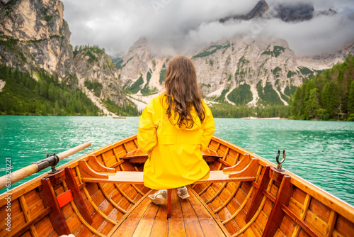 Woman sitting in big brown boat at Lago Braies lake in cloudy day, Italy. Summer vacation in Europe © dtatiana