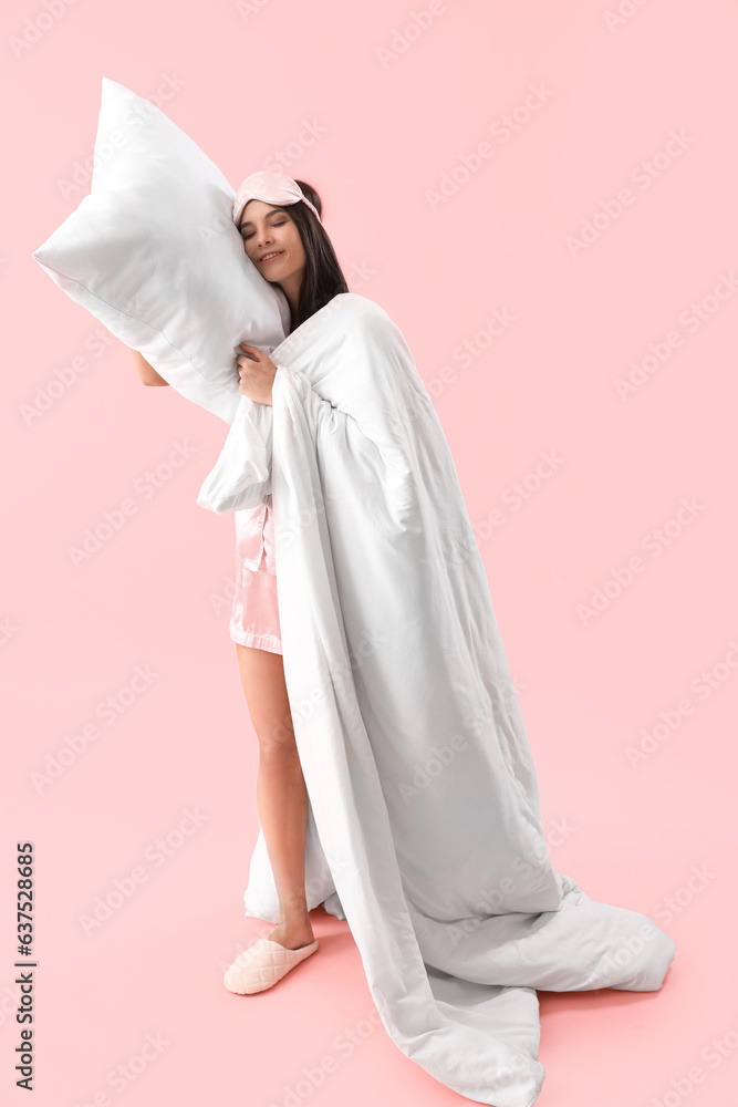 Beautiful young woman in pajamas with soft pillow and blanket sleeping on pink background