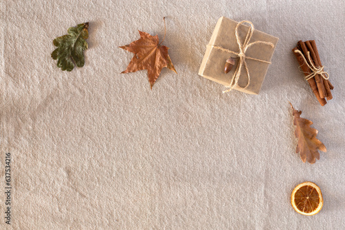 Autumn composition with autumn dry leaves, a gift wrapped in kraft paper, laid out in a corner on a rustic linen fabric background. Flat lay, top view, copy space