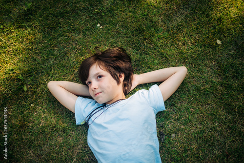 Smiling boy lying down with hands behind head on grass
