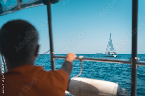 Sailing yacht cruising the azure waters of the Aegean Sea near Skopelos Island, with a man gripping the rail in the foreground and another vessel framing the picturesque scene.