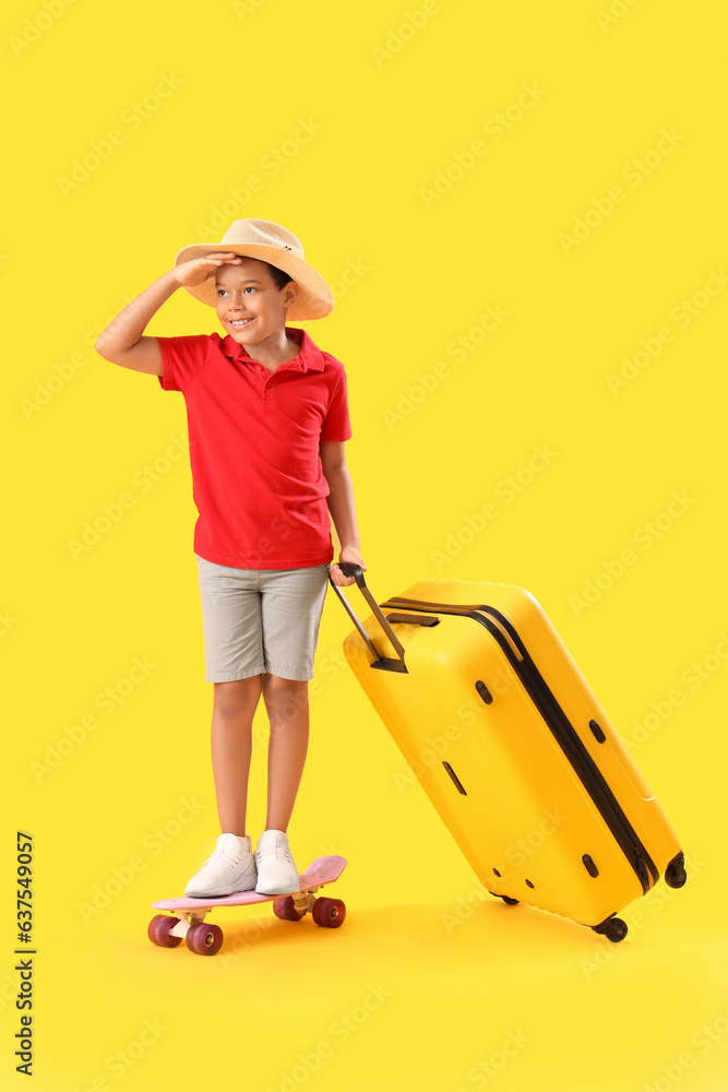 Little African-American boy with suitcase and skateboard on yellow background Little African-American boy with suitcase and skateboard on yellow background