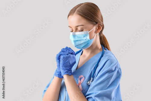 Female doctor with pink ribbon praying on light background. Breast cancer awareness concept