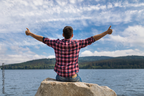 Happy Joyful Young Man Feeling Alive Joyful Positive Thumbs Up Sitting Next to a Beautiful Lake Enjoying Peaceful Nature