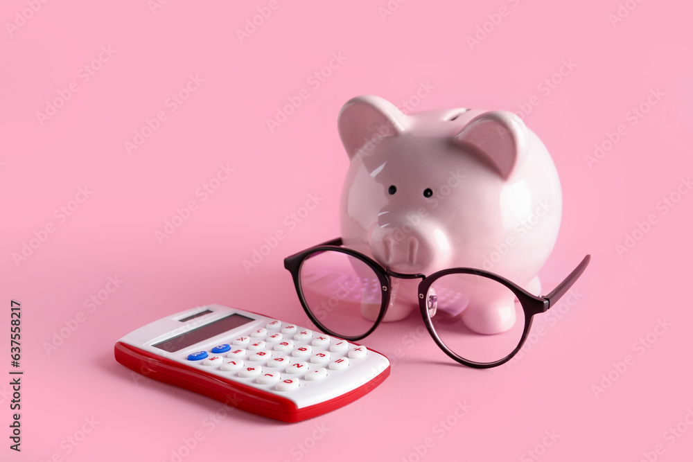Piggy bank with eyeglasses and calculator on pink background Piggy bank with eyeglasses and calculator on pink background