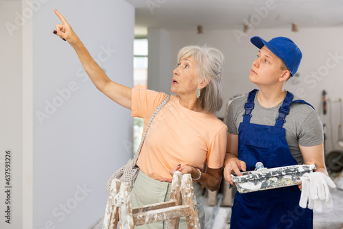 Obraz na plátně Senior woman employer explaining work details to teenager boy who working on part-time job in construction site as painter