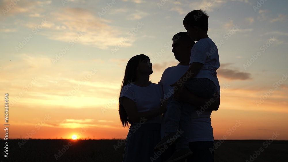 Happy young family hugging child son. Happy mom dad child, hugging, enjoying nature, sky silhouette. Father, mother, little boy in fathers arms, walking outdoors. Family plays together on summer field