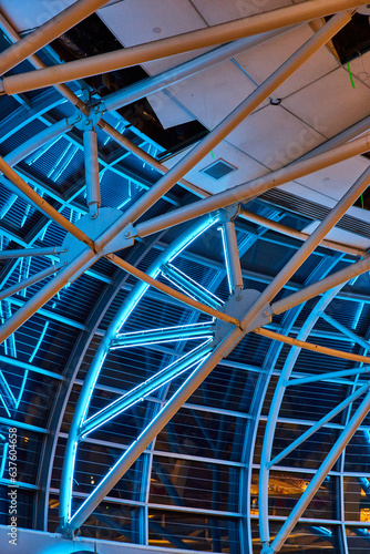 Curved wall of windows leading to ceiling with white beams illuminated by neon blue lights
