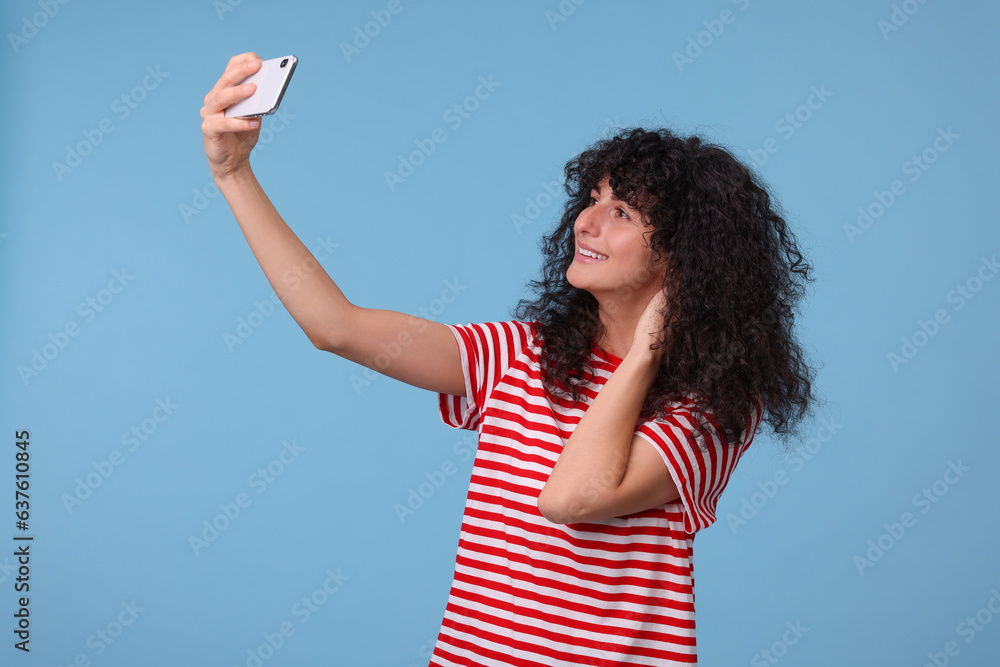 Beautiful young woman taking selfie on light blue background