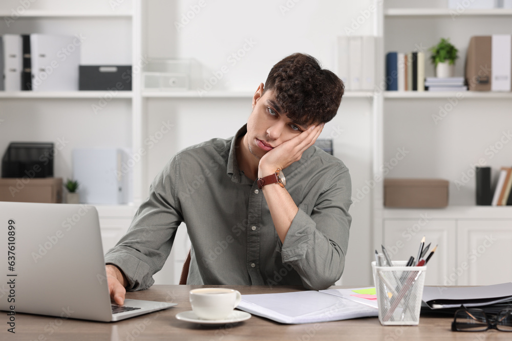 Tired young man working at table in office. Deadline concept Tired young man working at table in office. Deadline concept
