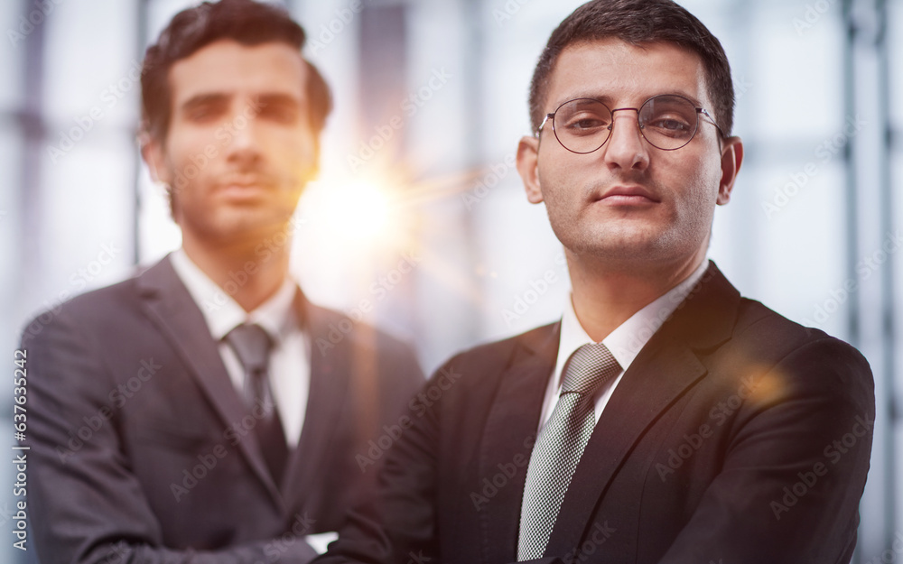Two serious young businessmen standing with arms crossed in office Two serious young businessmen standing with arms crossed in office