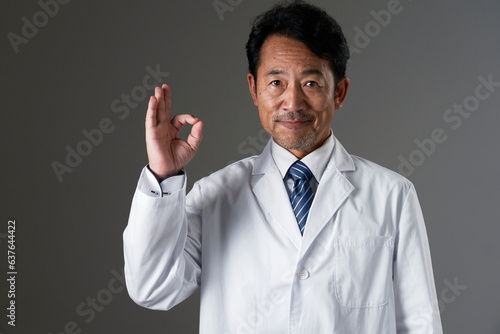 OKポーズをするミドルエイジの医者 黒背景