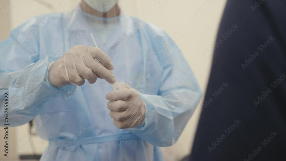 A medical professional in full protective gear prepares a swab test kit, ensuring accurate and safe sample collection from a patient in a clinical setting. A medical professional in full protective gear prepares a swab test kit, ensuring accurate and safe sample collection from a patient in a clinical setting.