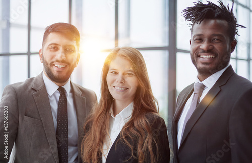 Three professionals in formal suits standing for camera indoors and smiling. Corporate friendship concept