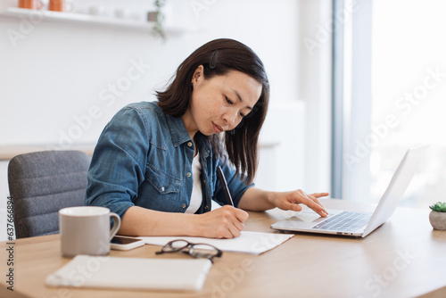 Lady putting down ideas on paper near at desk with laptop