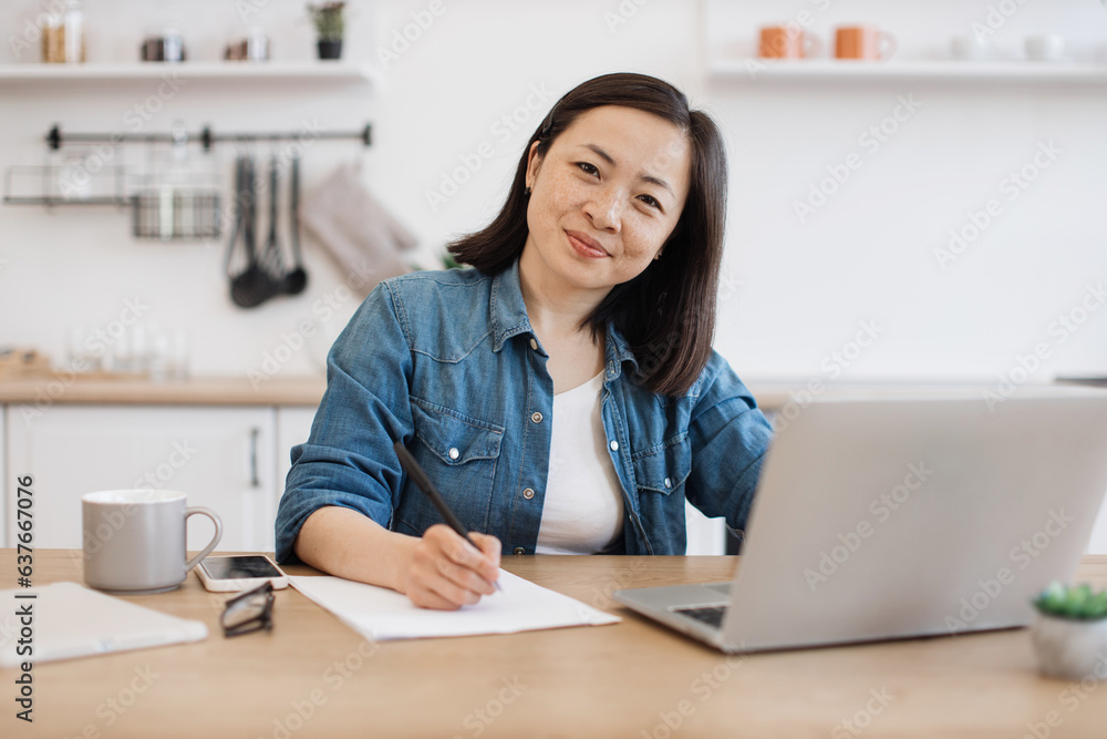 Lady putting down ideas on paper near at desk with laptop Lady putting down ideas on paper near at desk with laptop