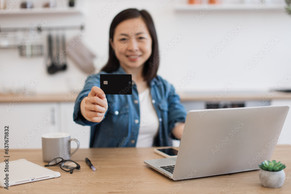 Black payment card held by asian lady working at home Black payment card held by asian lady working at home