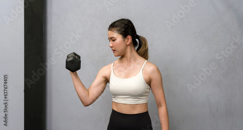 Fotografie A physically fit woman engaged in a workout session at a modern gym, determinedly lifting a heavy dumbbell as she strives for strength and wellness